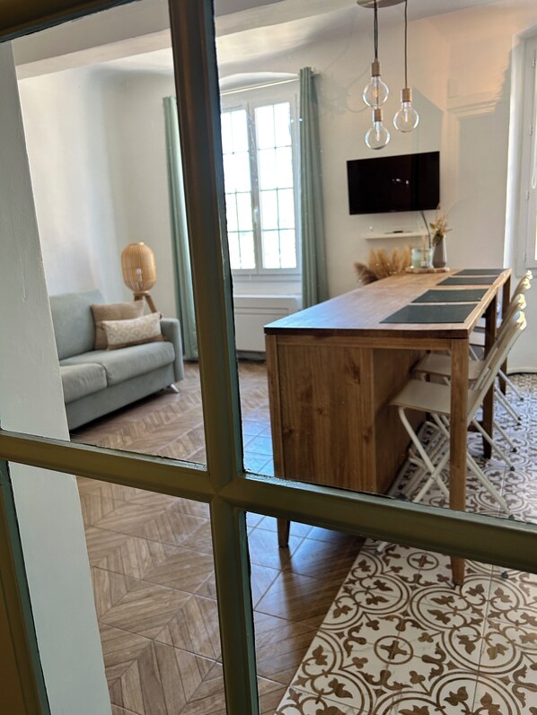 Un salon moderne comprenant un canapé, une table à manger avec des chaises, un téléviseur fixé au mur et un tapis à motifs.