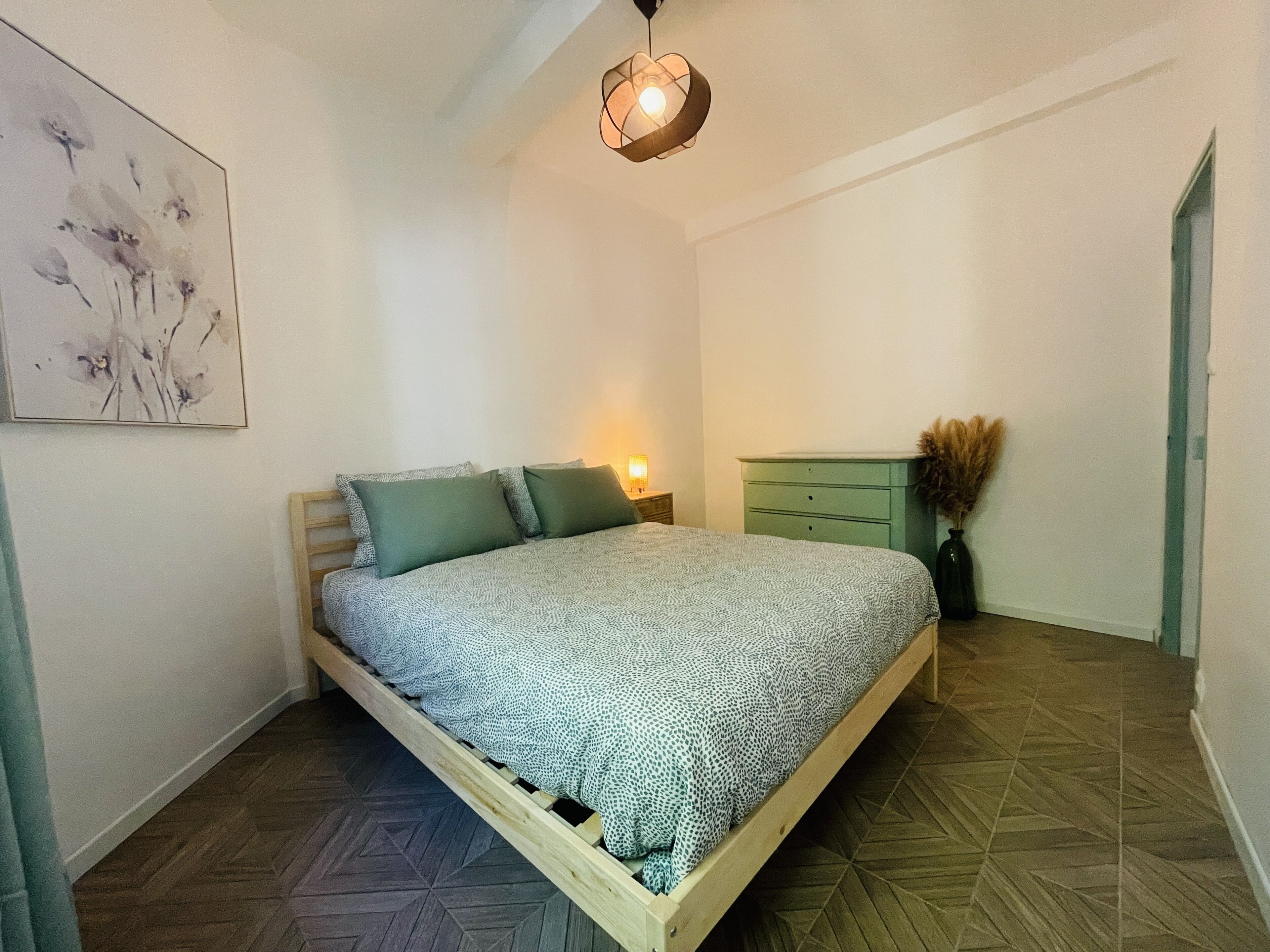 Un dormitorio con cama, mesita de noche, cómoda y lámpara colgante.