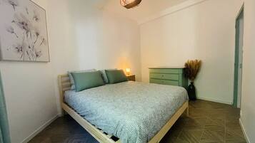 Un dormitorio con cama, mesita de noche, cómoda y lámpara colgante.