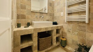 Une salle de bain avec un mur en pierre, un lavabo blanc, un miroir, un porte-serviettes et une poubelle.
