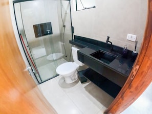 Casa de banho com chuveiro envidraçado, sanita branca e lavatório preto com espelho em cima.