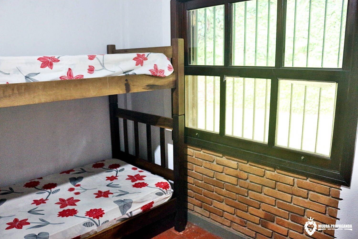 A bunk bed with floral bedding, a wooden headboard, and a window with vertical bars.