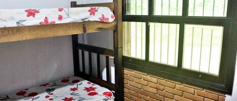A bunk bed with floral bedding, a wooden headboard, and a window with vertical bars.