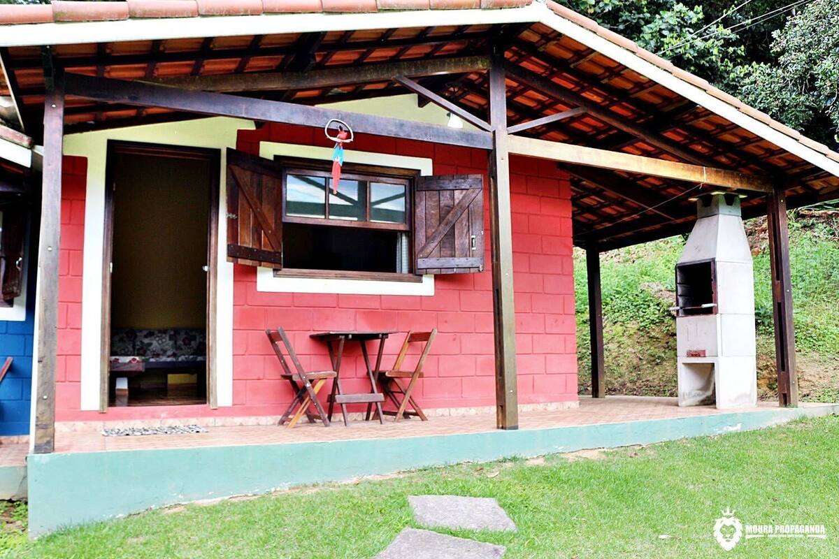 Een rood gebouw met een overdekte veranda, een raam met luiken en een barbecue.