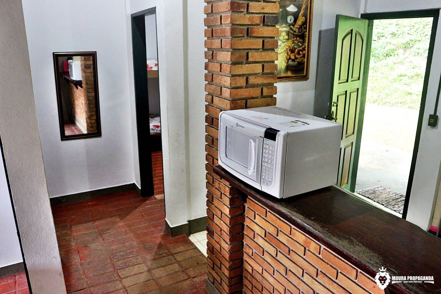 A kitchen with a microwave on a brick counter, a green door, and a framed picture on the wall.