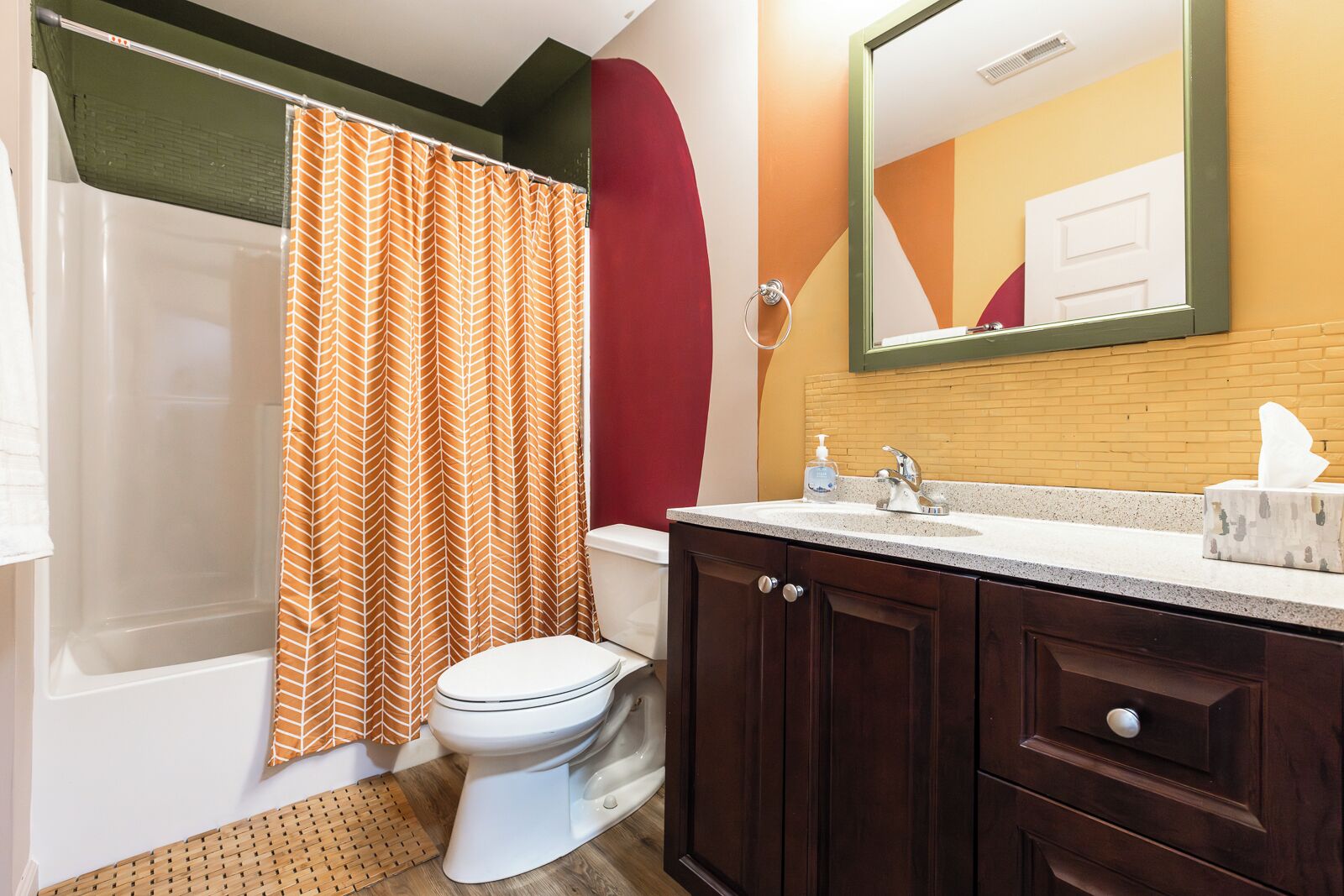A bathroom with a shower curtain, toilet, sink, and wooden cabinets.
