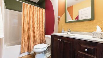 A bathroom with a shower curtain, toilet, sink, and wooden cabinets.