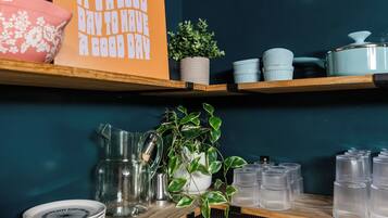 A kitchen shelf with a sign, a potted plant, a pitcher, and stacked cups.