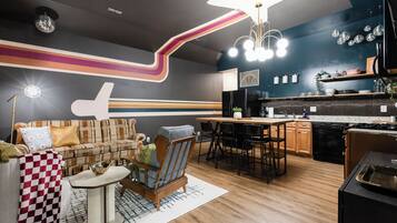 A modern living room with a sofa, armchairs, a dining table, and a kitchen area with a refrigerator, stove, and sink.