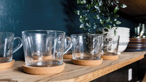 A wooden shelf with clear glass mugs on cork coasters.