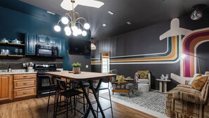 A modern kitchen with a dining area, featuring a wooden table, black chairs, and a large TV.