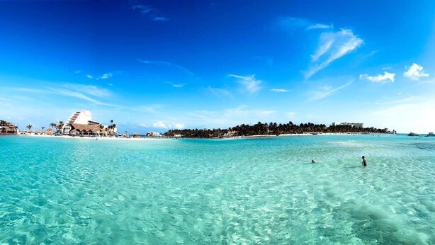 Een strandresort met helder turquoise water, een resortgebouw en een door palmbomen omzoomde kustlijn.