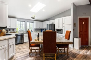 Una cocina moderna con armarios blancos, una mesa de comedor con sillas, un refrigerador y un lavavajillas.