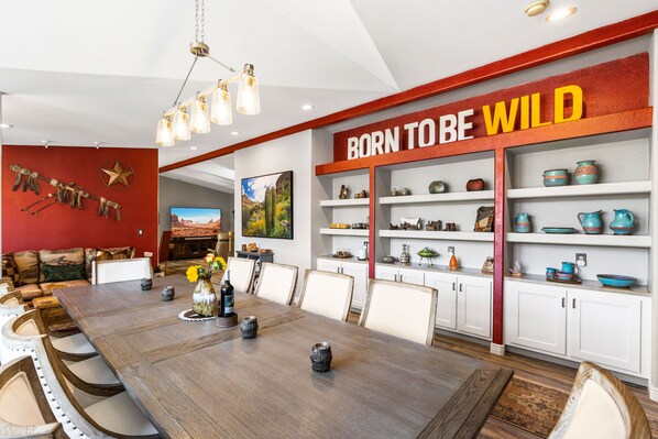 A spacious dining area with a long wooden table, white chairs, and a red accent wall with the phrase "BORN TO BE WILD".
