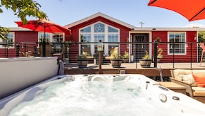 A hot tub area with a red building in the background, a fenced patio, and potted plants. - Cowboys & Roses - Wine Country Home w/Game Room, Hot Tub & Views - Dogs Welcome! (Cornville)