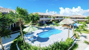 Ein Resort mit mehreren Gebäuden, deren Dächer aus Stroh sind, einem zentralen Schwimmbecken und Sitzbereichen im Freien.
