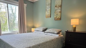 Quarto com cama, duas pinturas penduradas na parede, abajur e cômoda.