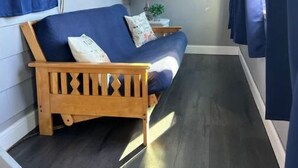 Um quarto acolhedor com um sofá de madeira, uma mesinha com abajur e uma janela com cortinas.
