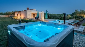 A hot tub with a stone exterior, a pool with lounge chairs, and a house with stone walls and a tiled roof. - Villa Silentio with Jacuzzi and Pool (Mali Vareški)