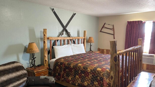 Ein rustikales Schlafzimmer mit einem hölzernen Bett, einem Holzstuhl, einem kleinen Tisch und einer an der Wand stehenden Leiter.