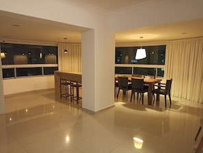 A modern hotel room with a dining area, large windows, and a chandelier. - AMPLO APARTAMENTO UM POR ANDAR (Balneário Camboriú)