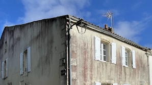 Un bâtiment à deux étages avec des volets blancs, une cheminée bien visible et une antenne métallique sur le toit.