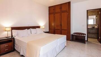 Habitación de hotel con cama, mesitas de noche, armario y baño visible a través de una puerta abierta.