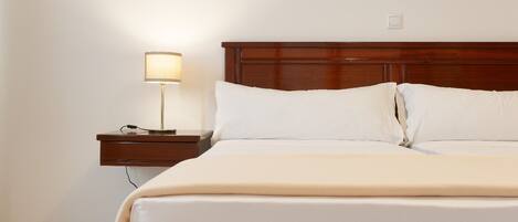 Una cama bien tendida con sábanas blancas y cabecera de madera en una habitación de hotel.