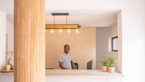 Un espace d’accueil avec un pilier en bois, un comptoir de réception, un ordinateur et deux plantes en pot.