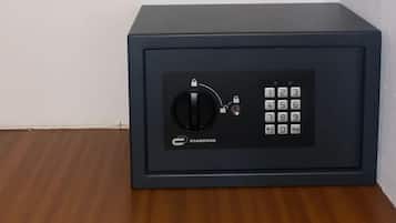 Um cofre preto com teclado numérico e fechadura combinada, colocado sobre um piso de madeira em frente a uma parede branca.