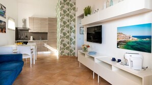 A modern living room with a TV, a dining area, and a kitchen. - Corrado Residence-Verde Blu - Apartment near beach (Reitani)