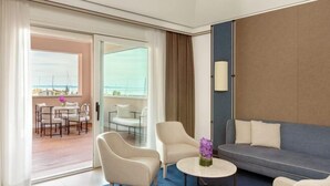 A modern hotel room with a sofa, two armchairs, a coffee table, and a view of the sea through a large window. - Tivoli Portopiccolo Sistiana Resort (Duino-Aurisina)