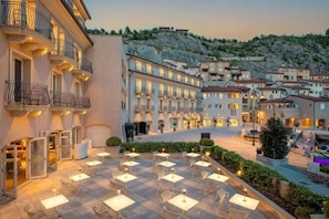 A courtyard with outdoor seating, buildings with balconies, and a hillside in the background. - Tivoli Portopiccolo Sistiana Resort (Duino-Aurisina)