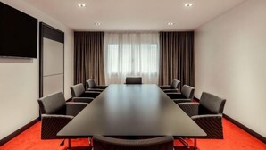 A conference room with a long table, multiple chairs, a projector screen, and curtains. - Tivoli Portopiccolo Sistiana Resort (Duino-Aurisina)