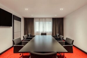 Una sala de conferencias con una larga mesa, varias sillas, una pantalla de proyector y cortinas.