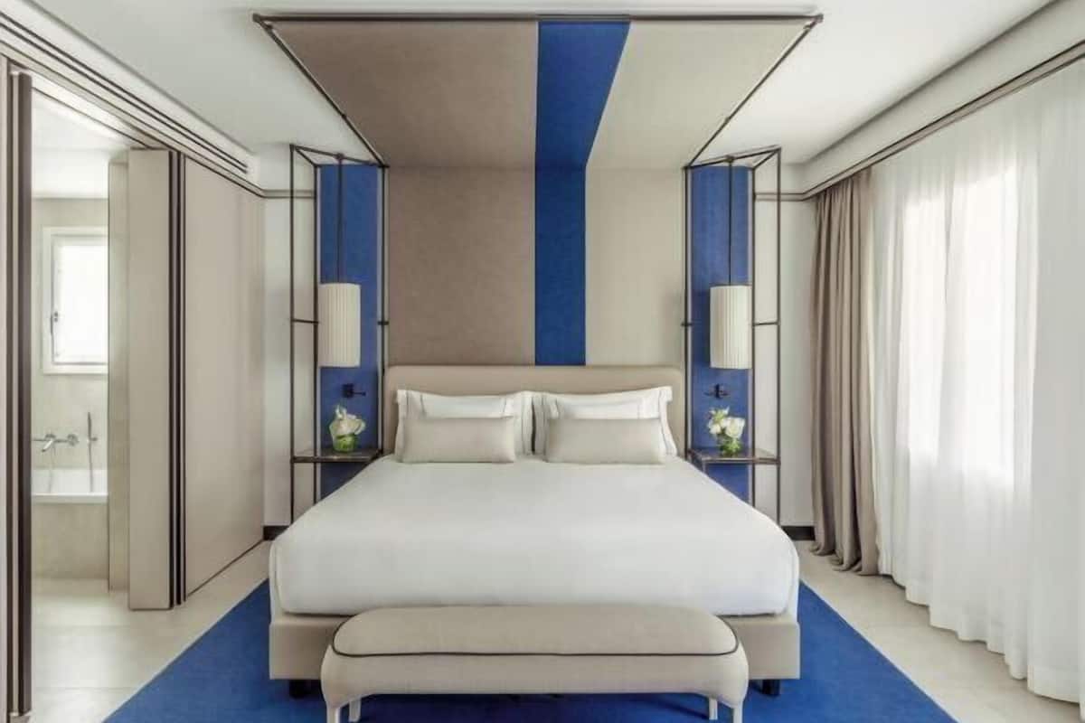 A modern hotel room with a large bed, a blue accent wall, and a neutral color scheme.