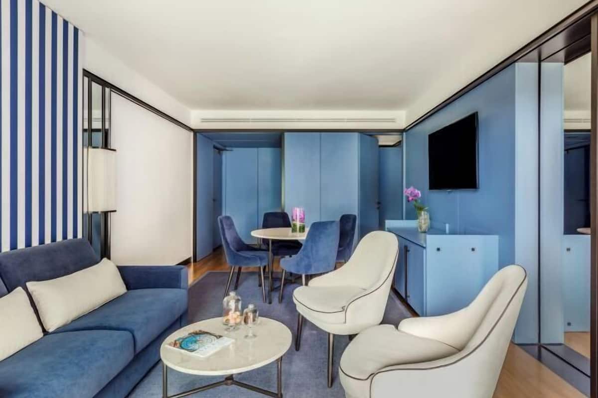 A modern living room with a blue sofa, a round coffee table, and a dining area with blue chairs.