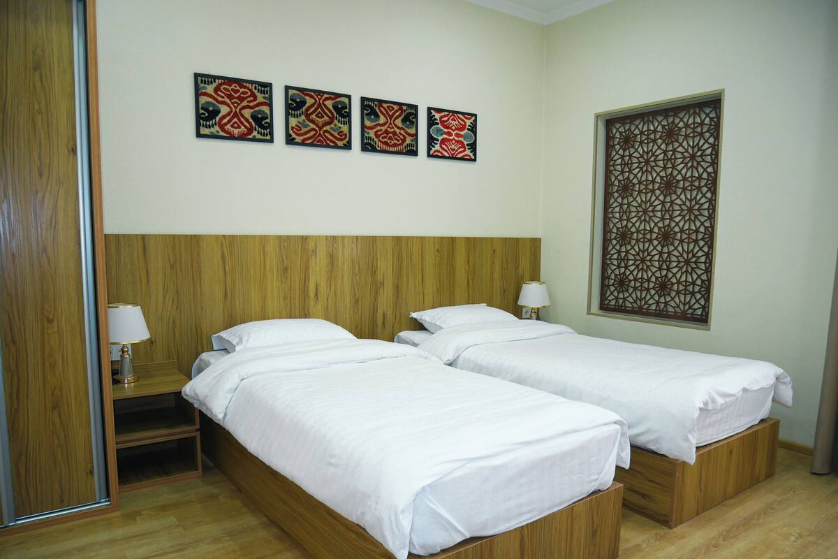Een hotelkamer met twee eenpersoonsbedden, houten hoofdeinden, een houten vloer en drie kunstwerken aan de muur.