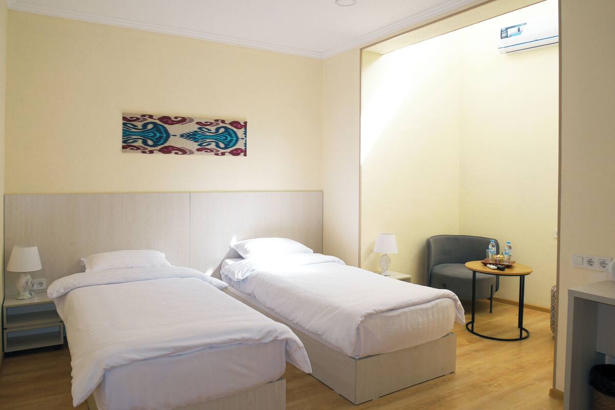 Hotelkamer met twee enkele bedden, een kleine tafel met stoel, een lamp en een wandairconditioner.
