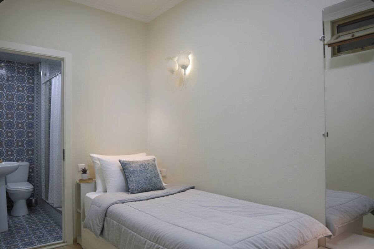 Een slaapkamer met een bed, nachtkastje, wandlamp en een badkamer met toilet en wastafel.