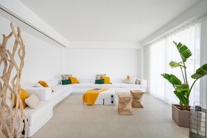 A modern living room with a white sectional sofa, yellow and green cushions, a wooden coffee table, and a large plant.