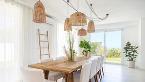 A dining area with a wooden table and white chairs, surrounded by wicker pendant lights. - Villa Finestrella, Seafront with pool (Arenella)