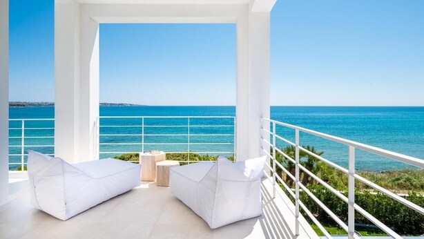 A balcony with white cushioned seating, a small table, and a view of the sea. - Villa Finestrella, Seafront with pool (Arenella)