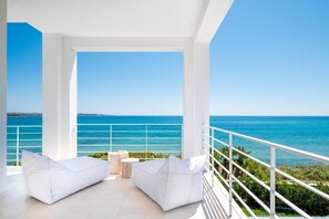 Un balcon doté de sièges rembourrés blancs, d’une petite table et offrant une vue sur la mer.