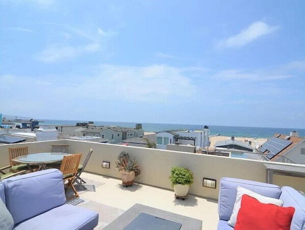 Enjoy the ocean view from this rooftop terrace, featuring a round table, comfortable seating, and lush greenery.