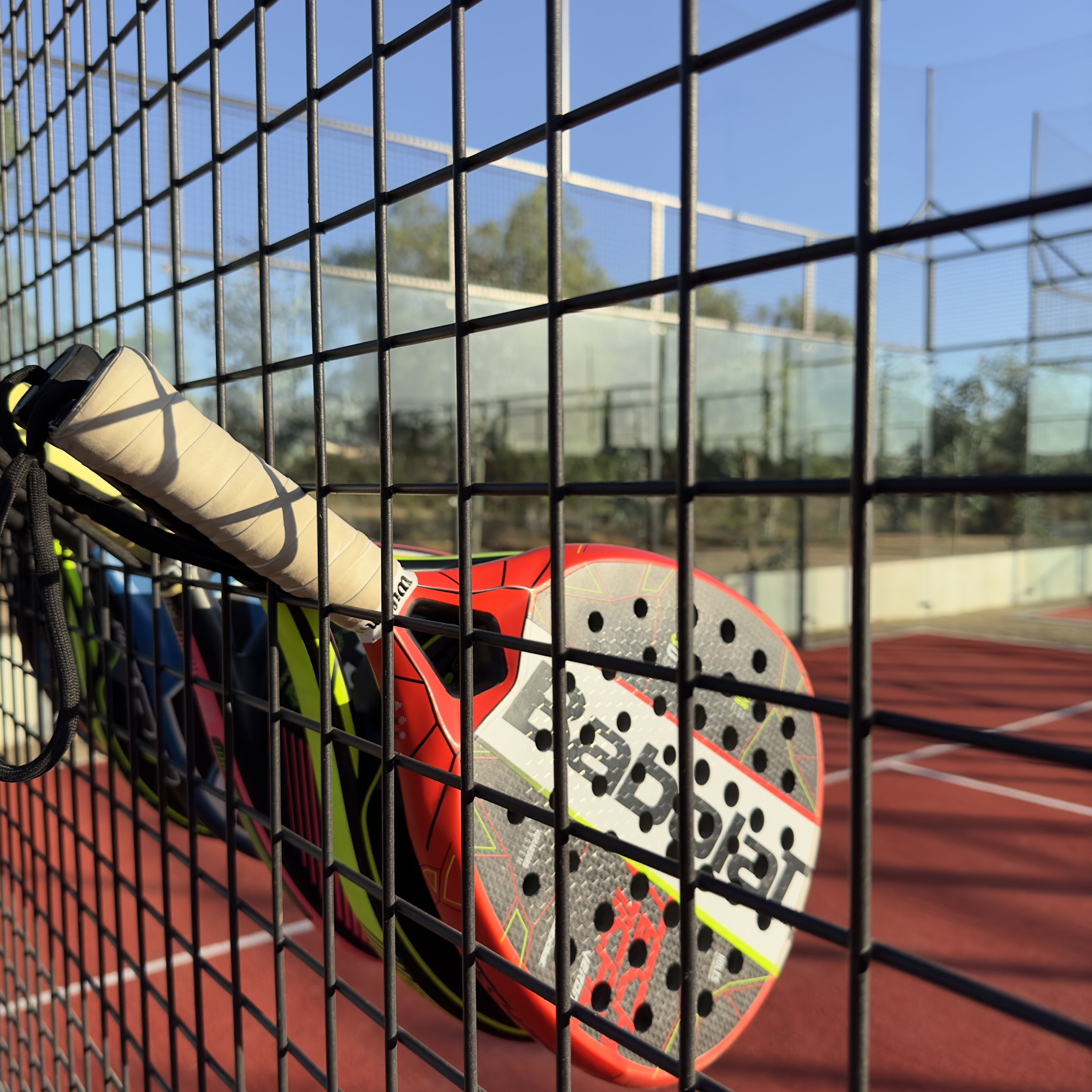 Una raqueta de tenis apoyada en una valla en una cancha de tenis.
