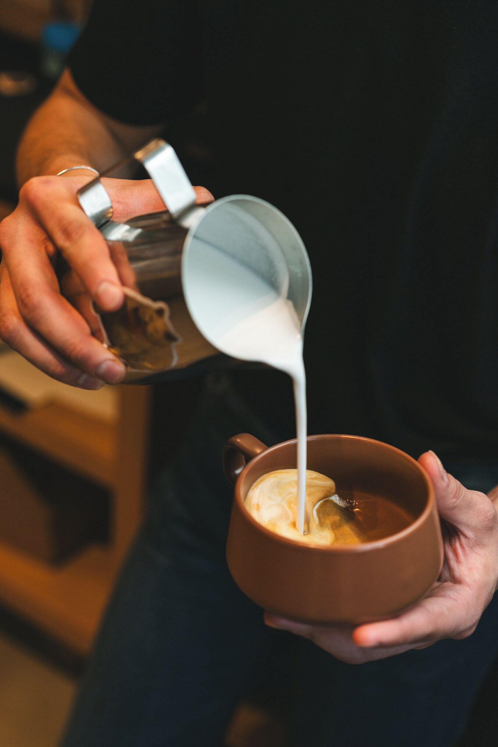 Una persona vertiendo leche en una taza de café.