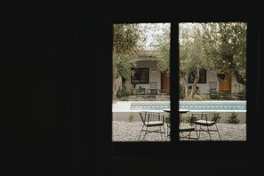A view through a window of a courtyard with a pool, outdoor seating, and greenery.