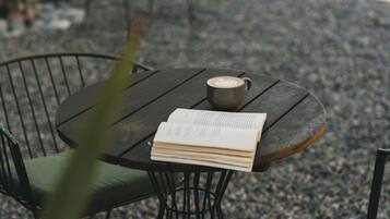 Une table ronde avec un livre et une tasse, entourée de chaises avec des coussins, dans un cadre extérieur agrémenté de gravier et de plantes.