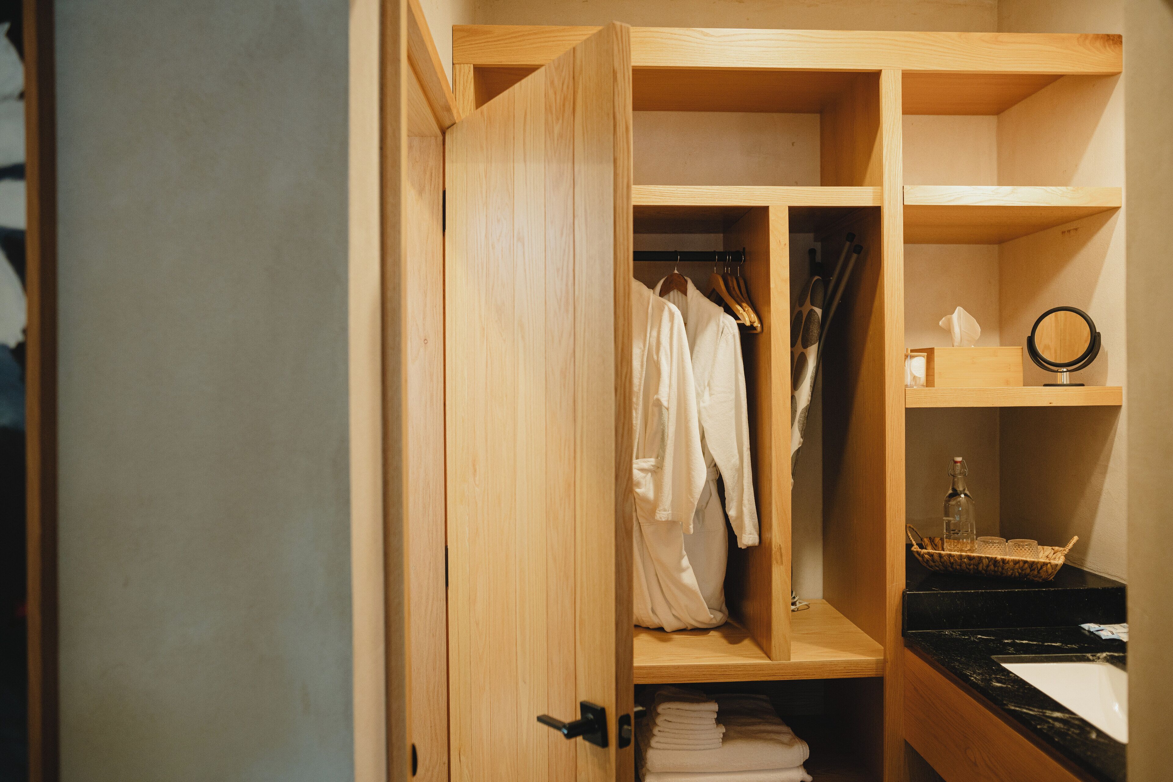 A wooden closet with hanging clothes, shelves, and a mirror.